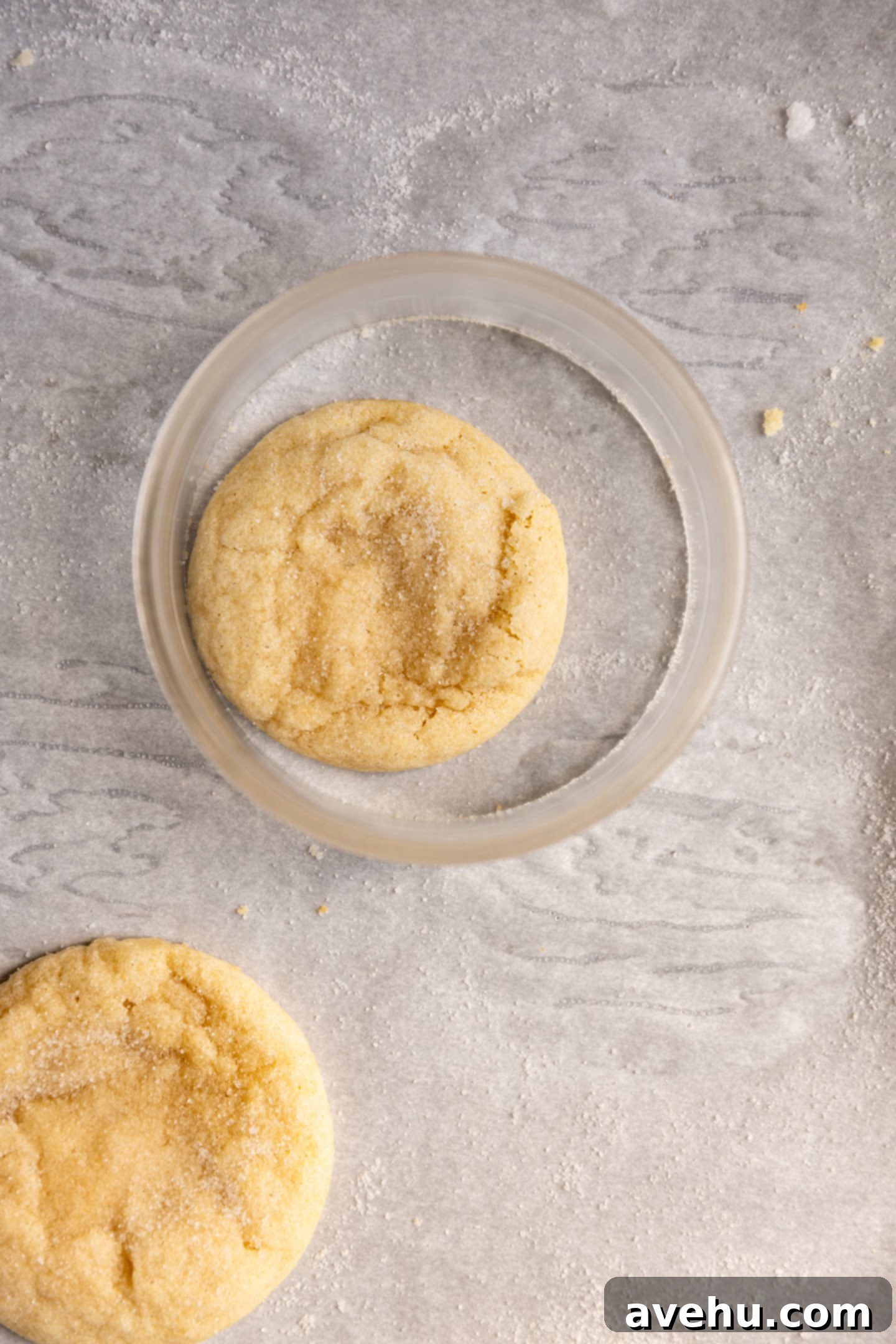 20-Minute Mixer-Free Sugar Cookies 9 A warm, freshly baked sugar cookie on parchment paper with a larger round cookie cutter placed around it, illustrating the 'scoot' technique.