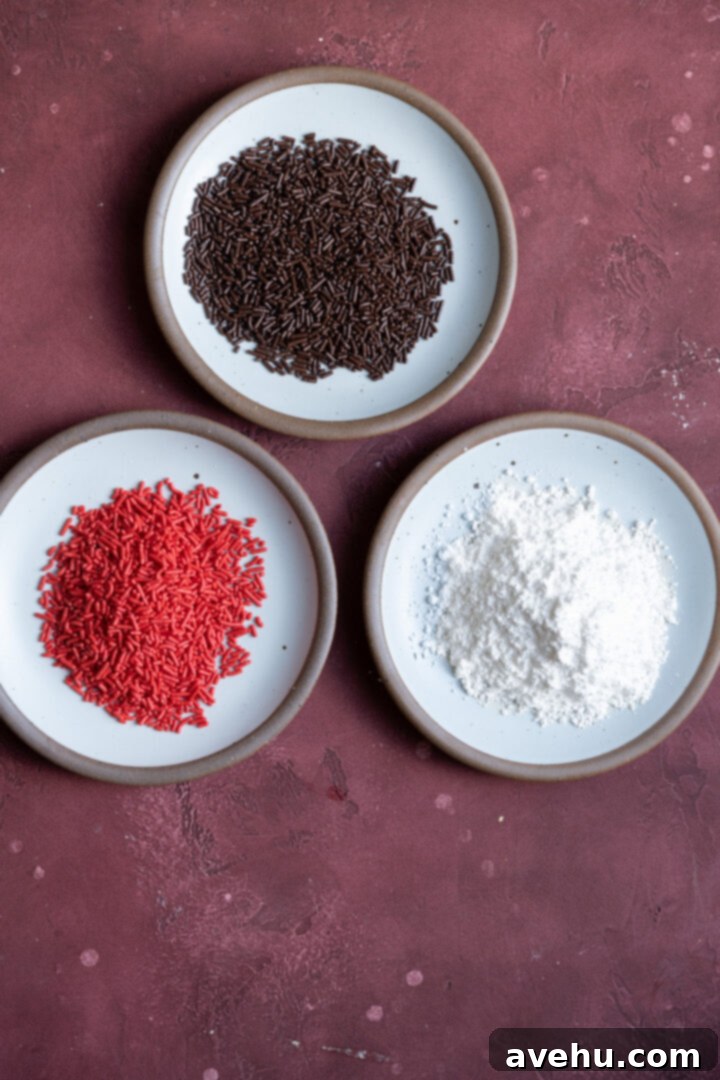 20-Minute Boozy Festive Rum Ball Recipe 9 Three plates of assorted toppings (sprinkles, coconut, powdered sugar) for rum balls on a burgundy surface.