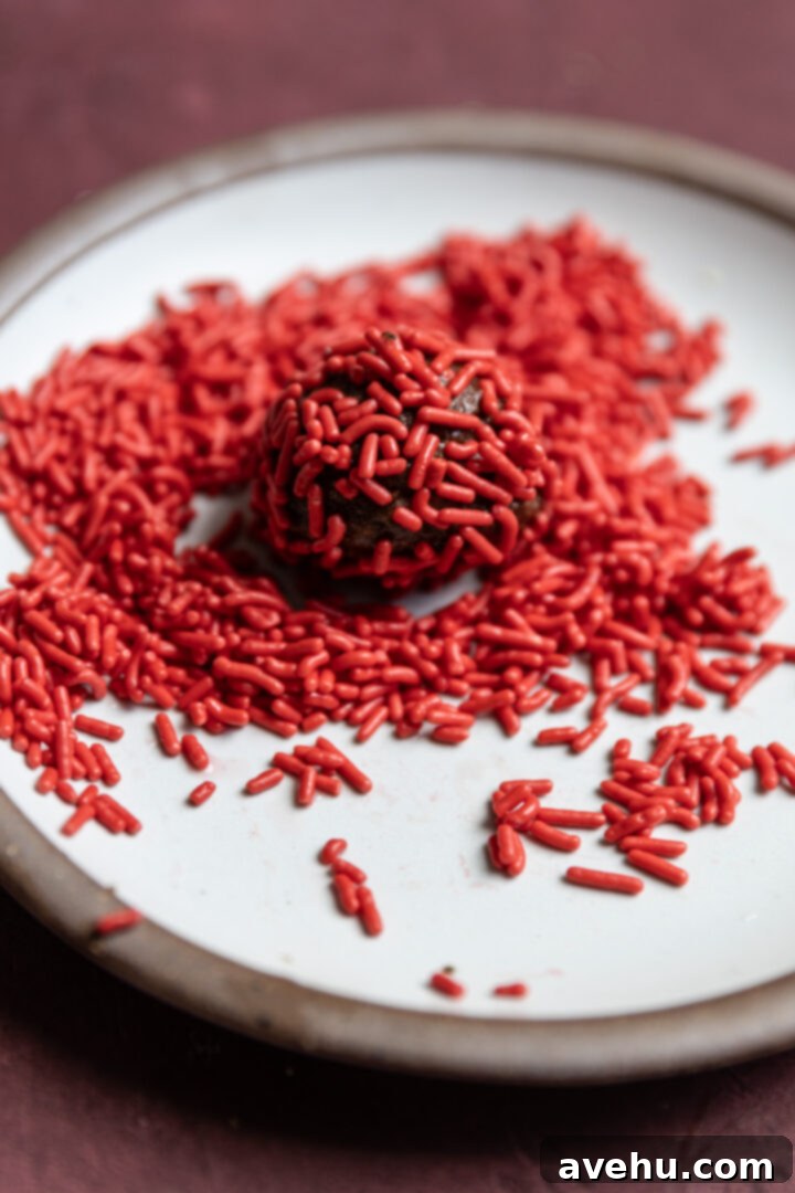 20-Minute Boozy Festive Rum Ball Recipe 10 A rum ball rolled in vibrant red sprinkles, placed on a white plate.