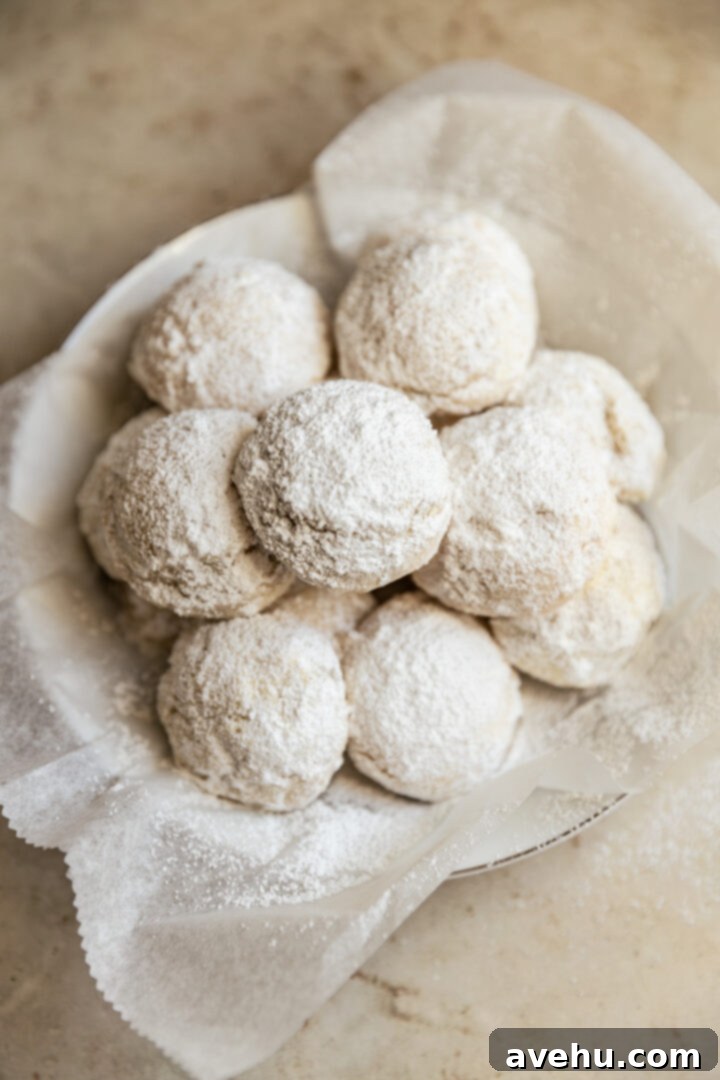 Effortless 3-Ingredient Snowball Cookies 2 Snowball cookies in a white bowl that is lined with parchment paper.