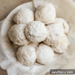 Effortless 3-Ingredient Snowball Cookies 12 Snowball cookies in a white bowl that is lined with parchment paper.