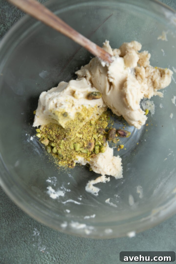 Effortless 3-Ingredient Snowball Cookies 7 Pistachios added to cookie dough in a glass bowl.
