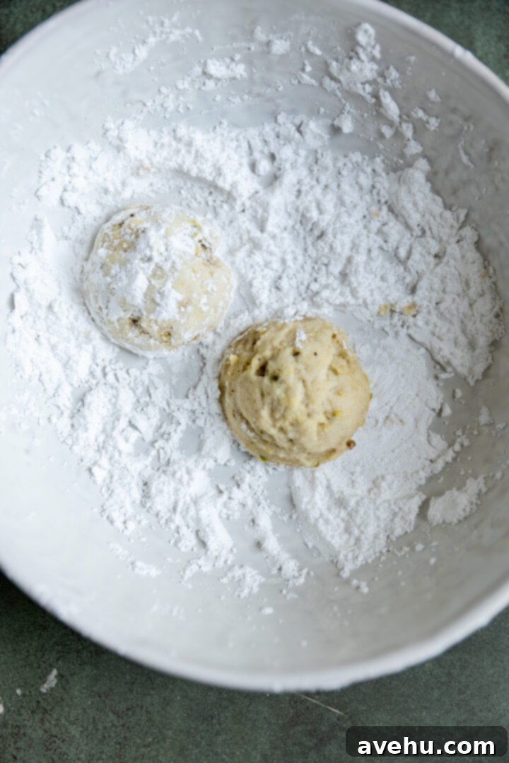 Effortless 3-Ingredient Snowball Cookies 10 Cookies rolled in powdered sugar in a bowl.