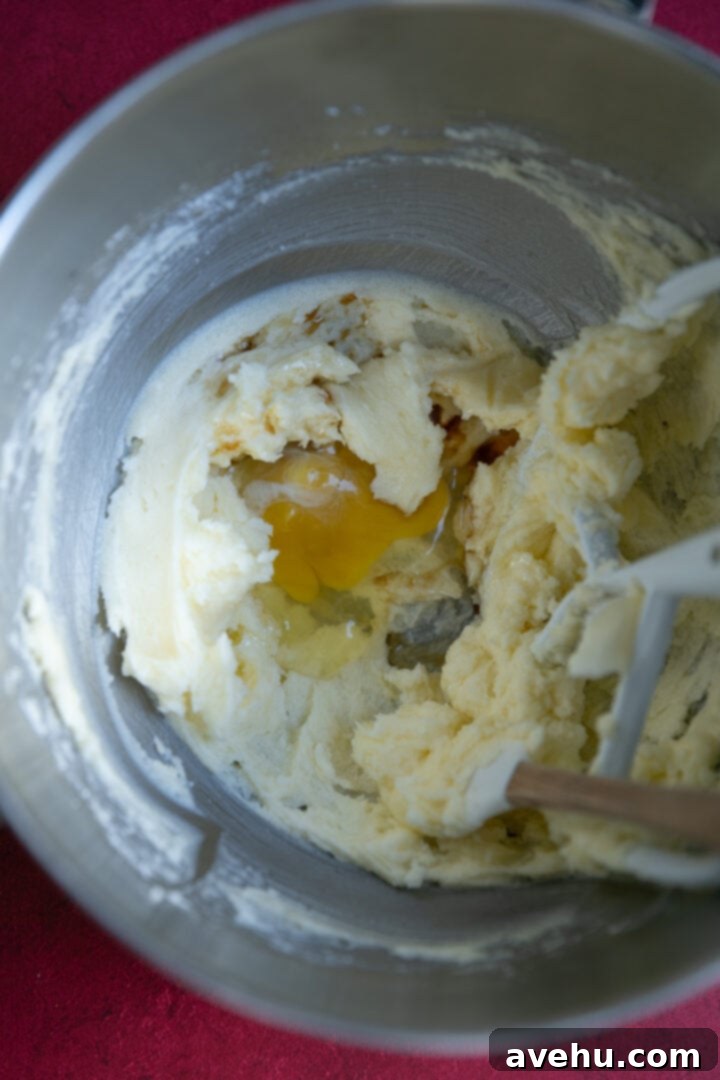Instant Cut-Out Sugar Cookies 5 An egg being added to the creamy butter and sugar mixture in a mixing bowl.