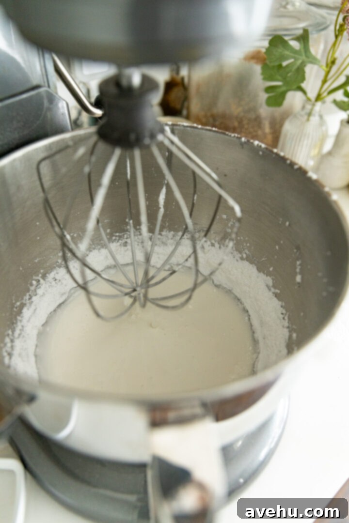 Quick Royal Icing Without Meringue Powder 5 A stand mixer with the whip attachment lifted to show icing inside.