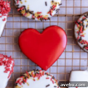 Quick No-Piping Cookie Icing 13 A red heart Iced sugar cookie next to other cookies with sprinkles on a wire rack.