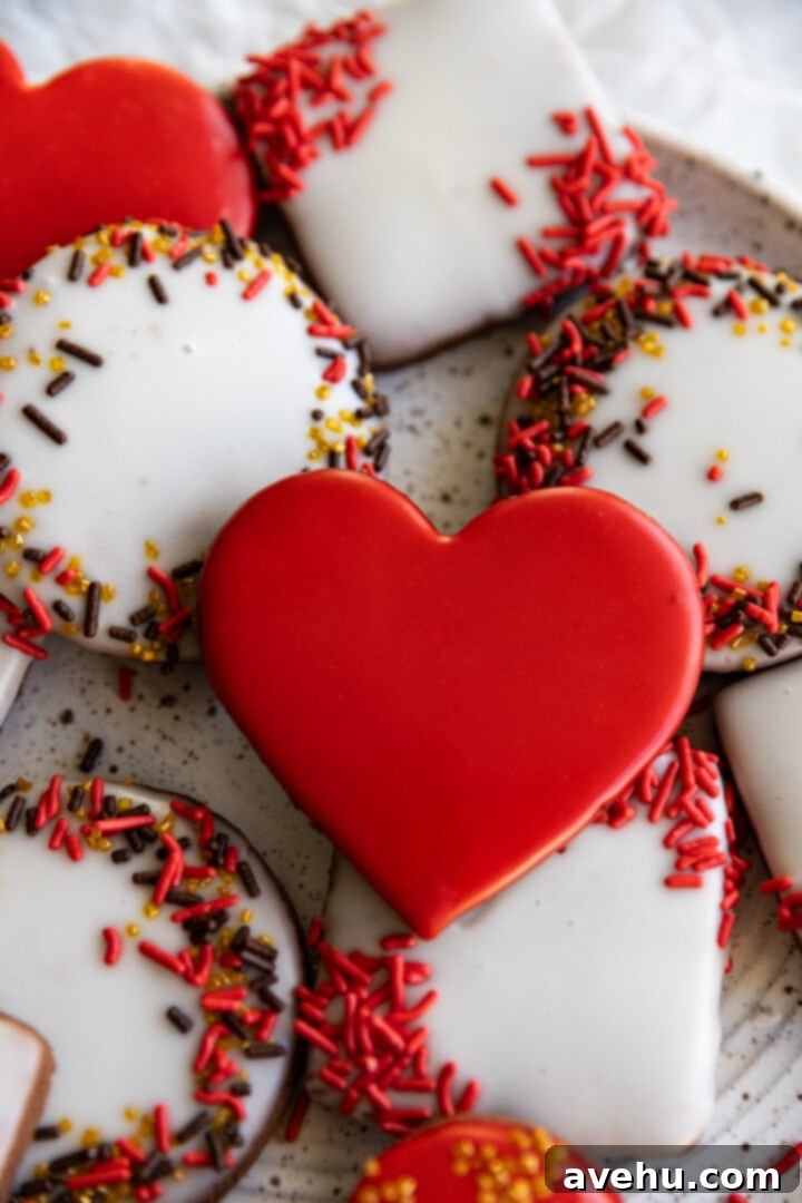 Instant Chocolate Sugar Cookie Delight 12 A vibrant red heart-shaped chocolate sugar cookie, surrounded by an assortment of sprinkle-decorated cookies, all frosted with easy cookie icing, presented on a white plate.