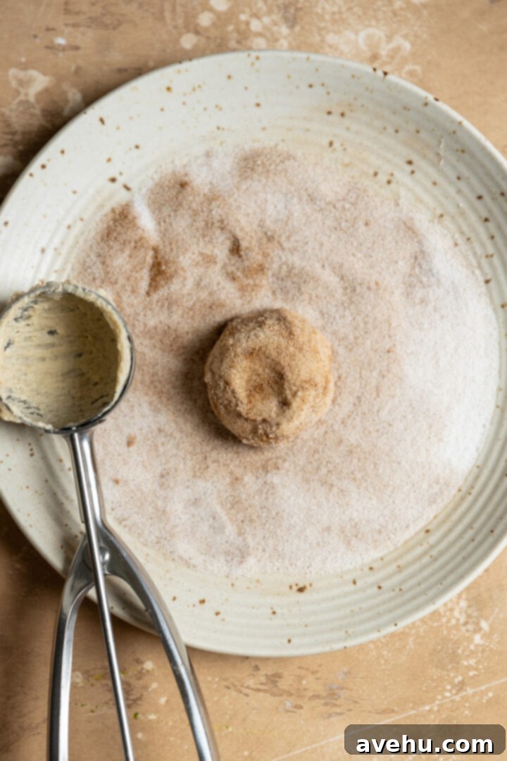 Cinnamon Sugar Chews in Minutes 6 A ball of cookie dough being rolled in a bowl of cinnamon sugar, showing an even coating.
