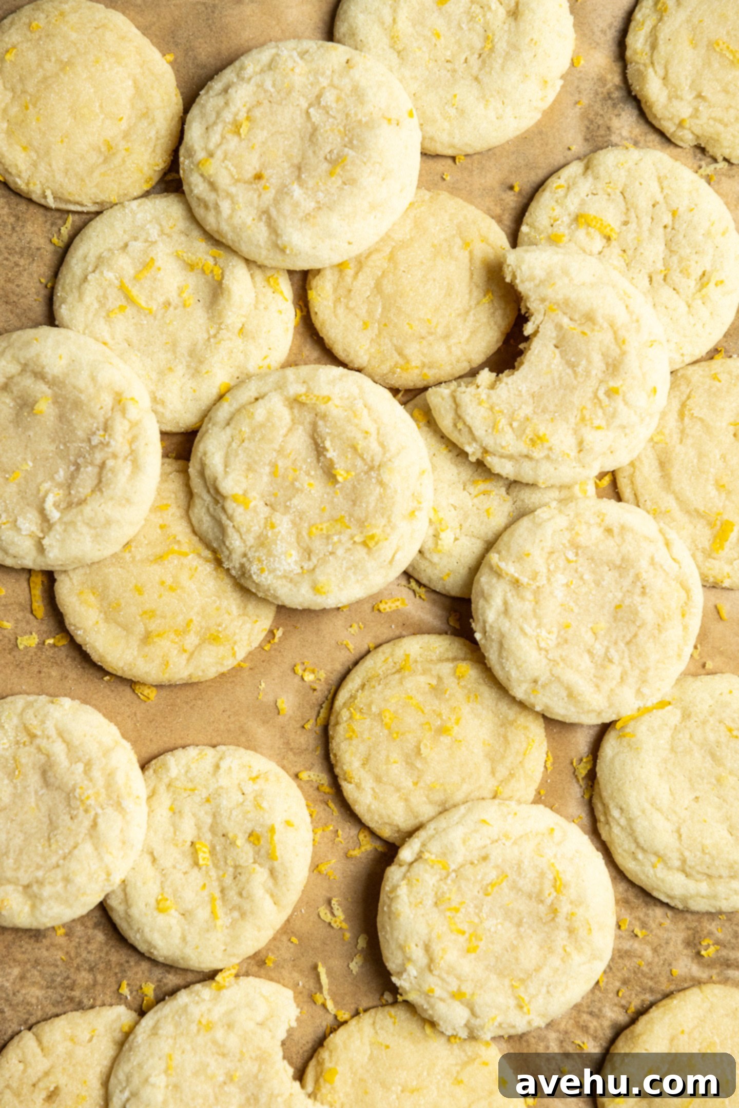 Zesty No-Chill Lemon Sugar Cookies 2 A bunch of lemon cookies scattered over parchment paper with one with a bite taken out if it.