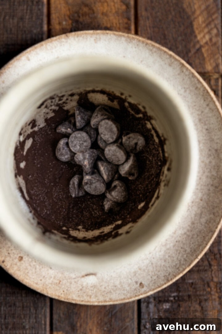 Instant Comfort Microwave Hot Cocoa for One 3 Cocoa powder, granulated sugar, and dark chocolate chips are visibly mixed together at the bottom of a ceramic mug, ready for the hot milk to be added.