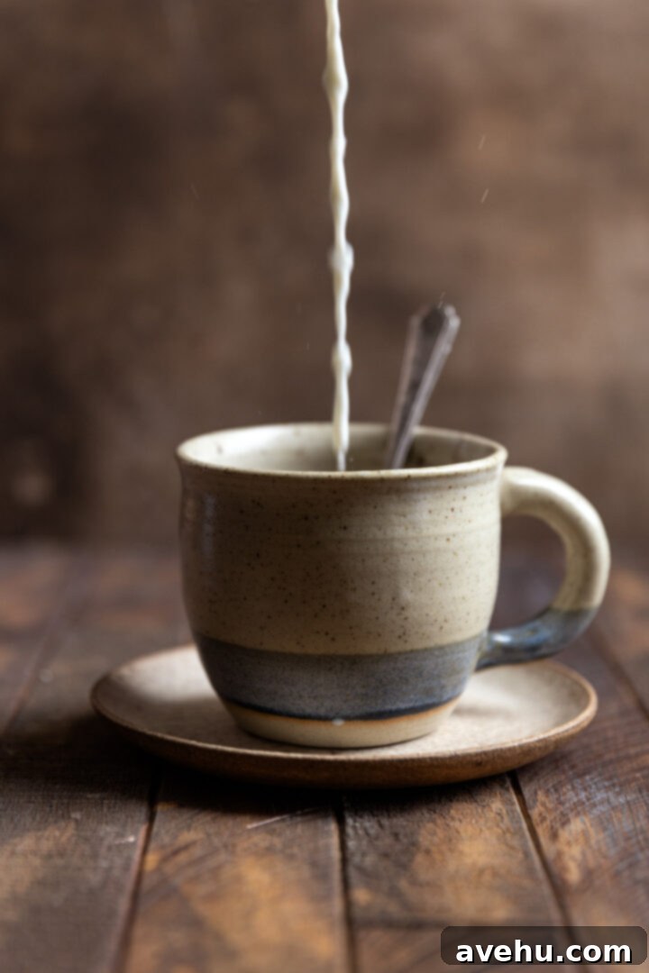 Instant Comfort Microwave Hot Cocoa for One 5 Hot milk is being poured from a measuring cup into a mug already containing the dry hot chocolate ingredients, creating a swirl of chocolate and milk as they begin to combine.