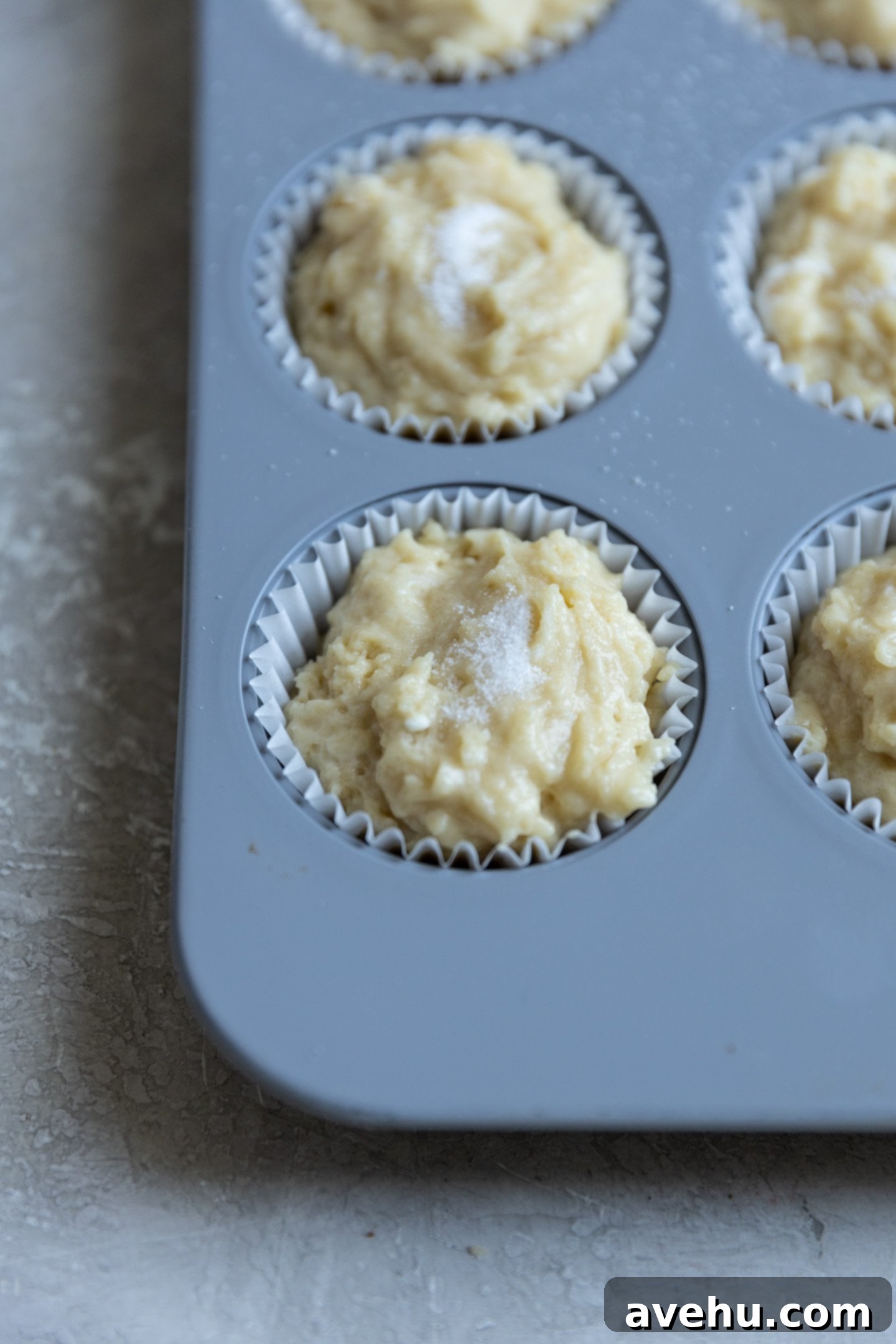 Classic Soft & Moist Muffins 7 Sugar sprinkled on top of muffin batter in a muffin tin.