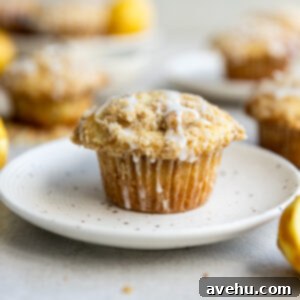 Gourmet Triple Lemon Muffins 13 A delicious triple lemon muffin, perfectly domed and glazed, resting on a white spotted plate, with more muffins in the background.