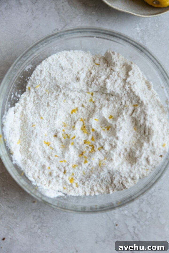 Gourmet Triple Lemon Muffins 5 Dry ingredients for lemon muffins, including flour, sugar, and lemon zest, in a glass bowl.