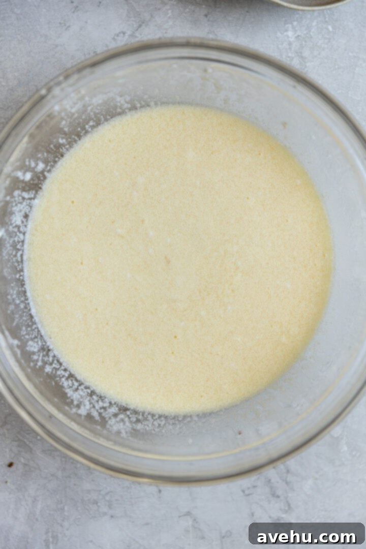 Gourmet Triple Lemon Muffins 6 Wet ingredients for lemon muffins, including eggs, milk, and oil, being whisked in a bowl.