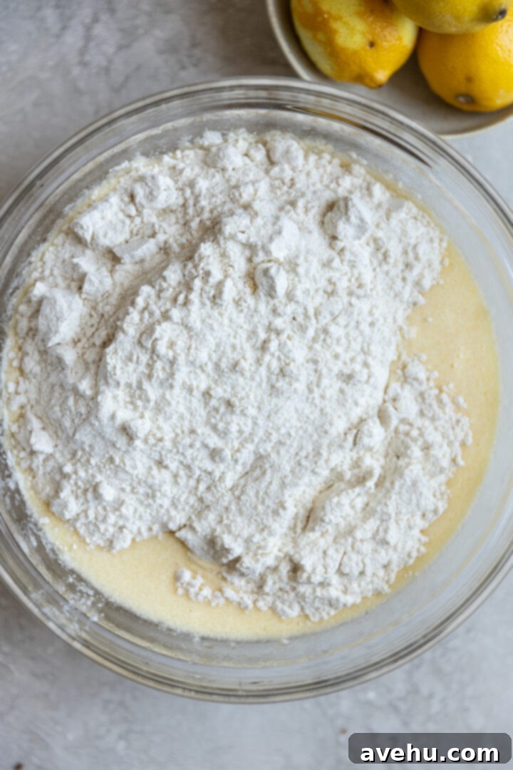 Gourmet Triple Lemon Muffins 7 Dry ingredients for lemon muffins being poured over wet ingredients in a bowl, demonstrating the proper mixing technique.