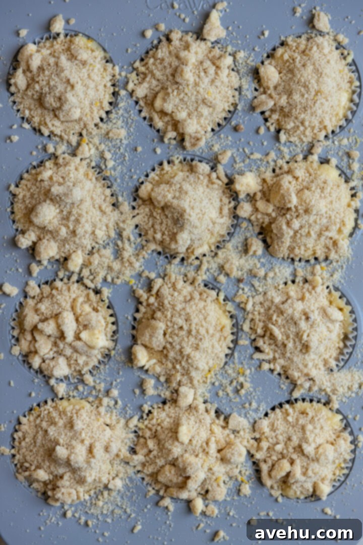Gourmet Triple Lemon Muffins 10 Generous amount of lemon streusel sprinkled over muffin batter in a muffin tin before baking, overflowing slightly.