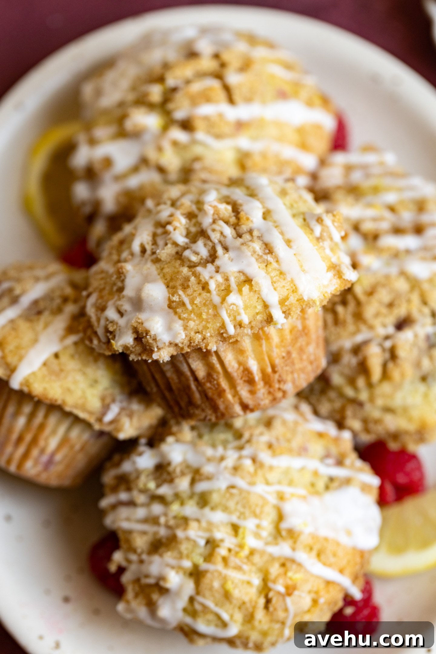 Luminous Lemon Raspberry Muffins 2 Freshly baked lemon raspberry muffins stacked on top of each other on a delicate pink plate, showcasing their golden tops and visible raspberry pieces.