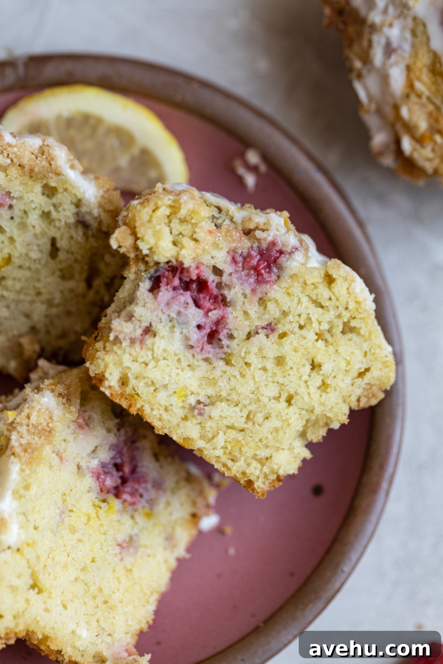 Luminous Lemon Raspberry Muffins 11 A freshly baked lemon raspberry muffin, sliced in half, revealing its moist interior packed with raspberries and zest, resting on a pink plate.