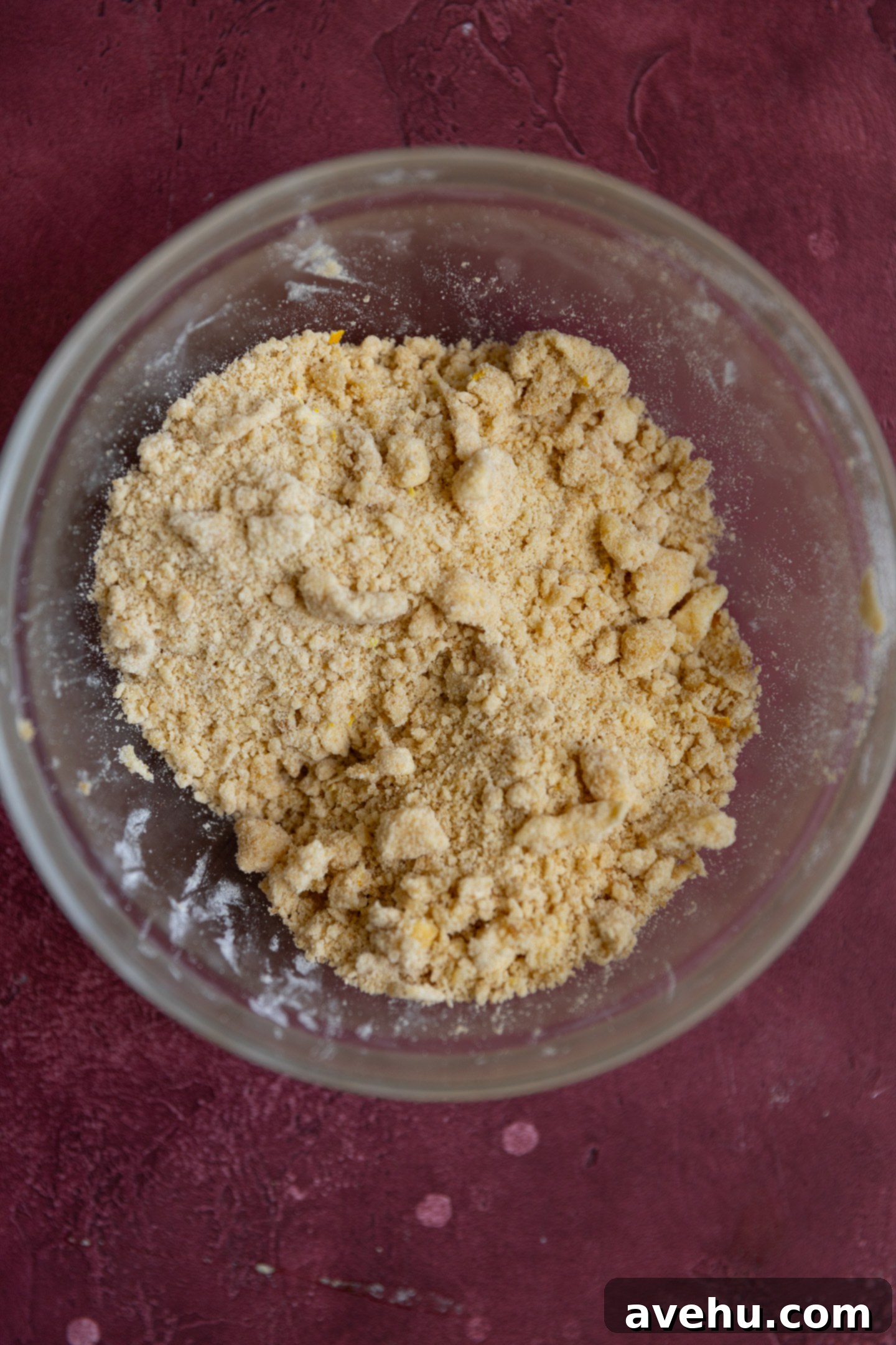 Luminous Lemon Raspberry Muffins 3 Close-up of lemon streusel mixture in a clear glass bowl, showing the small, crumbly pieces of butter mixed with dry ingredients.