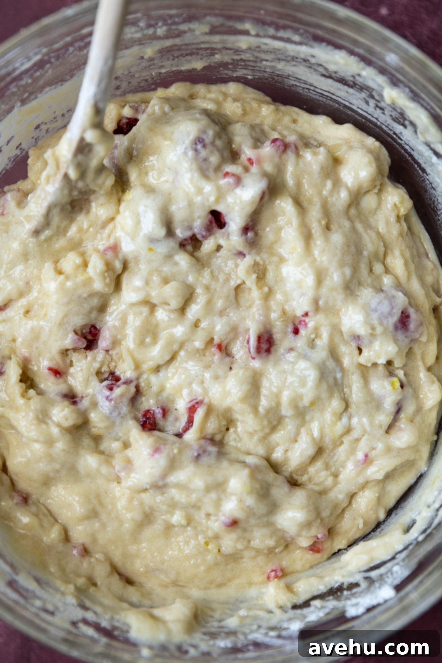 Luminous Lemon Raspberry Muffins 7 Lumpy lemon raspberry muffin batter in a bowl, mixed with a spatula, with small streaks of flour still visible.