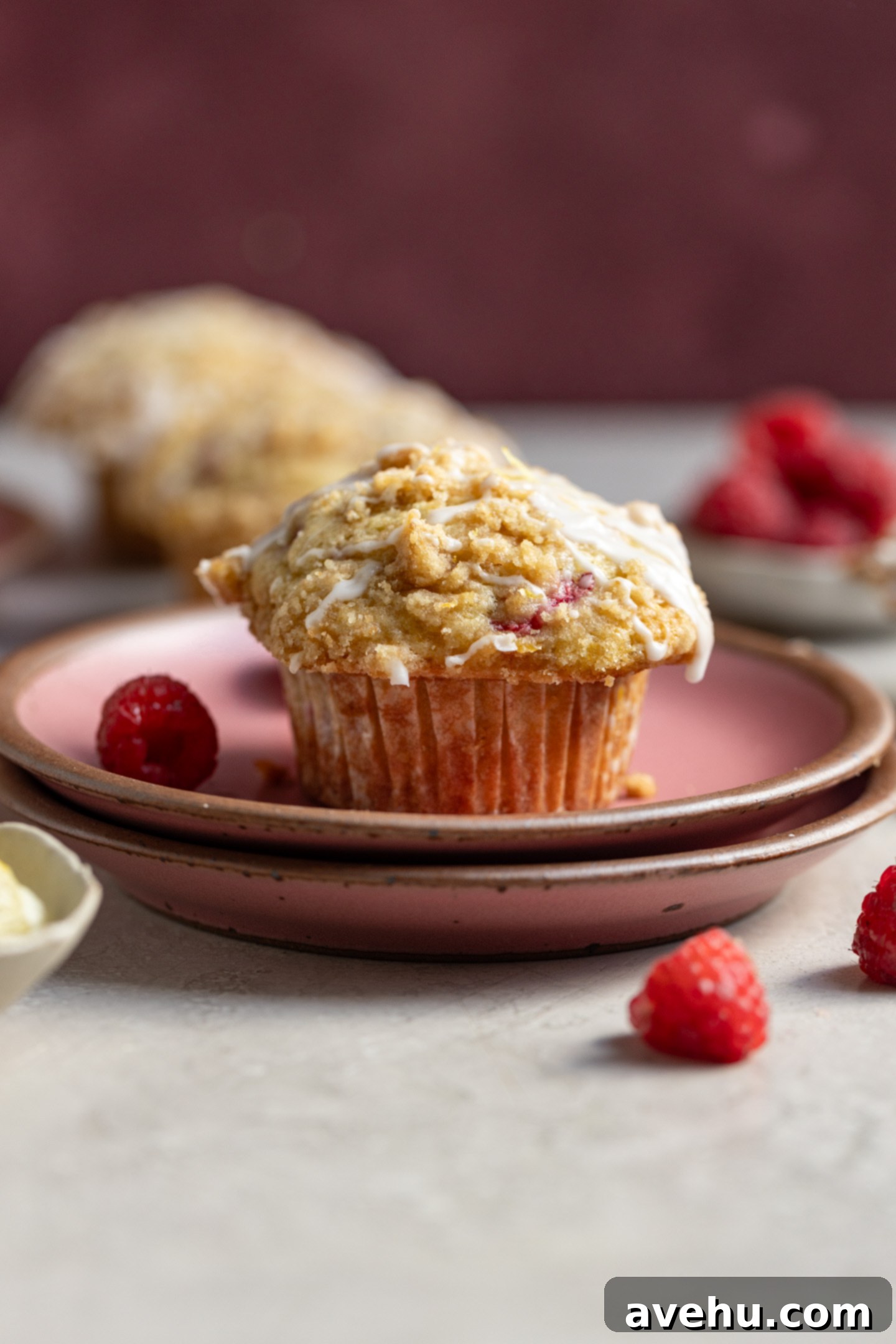 Luminous Lemon Raspberry Muffins 10 A single perfectly baked lemon raspberry muffin with a golden streusel top and a hint of glaze, resting on two stacked pink plates.
