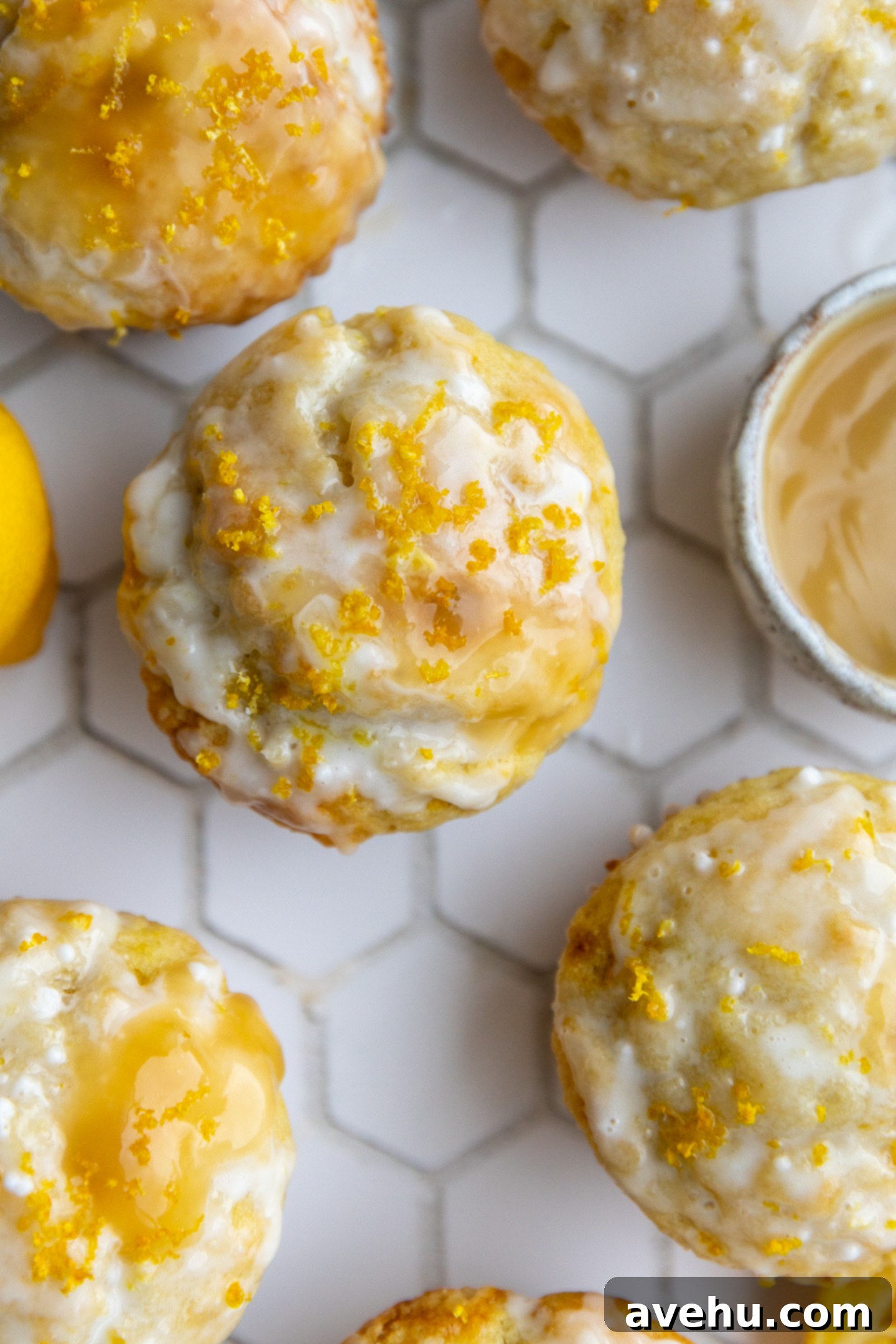 Pillowy Lemon Curd Muffins 12 Lemon curd muffins next to each other on a white hexagon design surface.