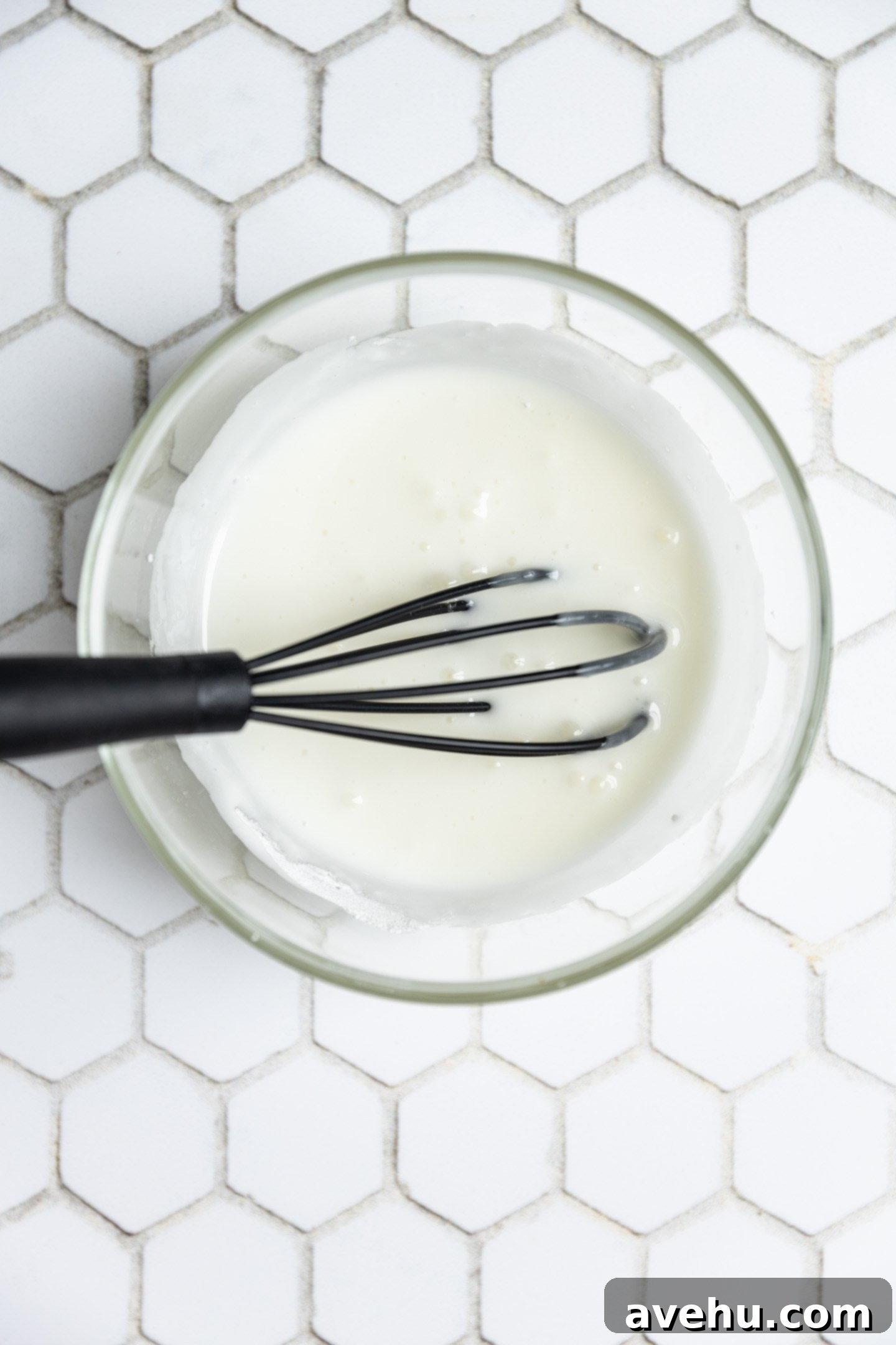 Pillowy Lemon Curd Muffins 10 Lemon glaze in a bowl on a white tiled surface.