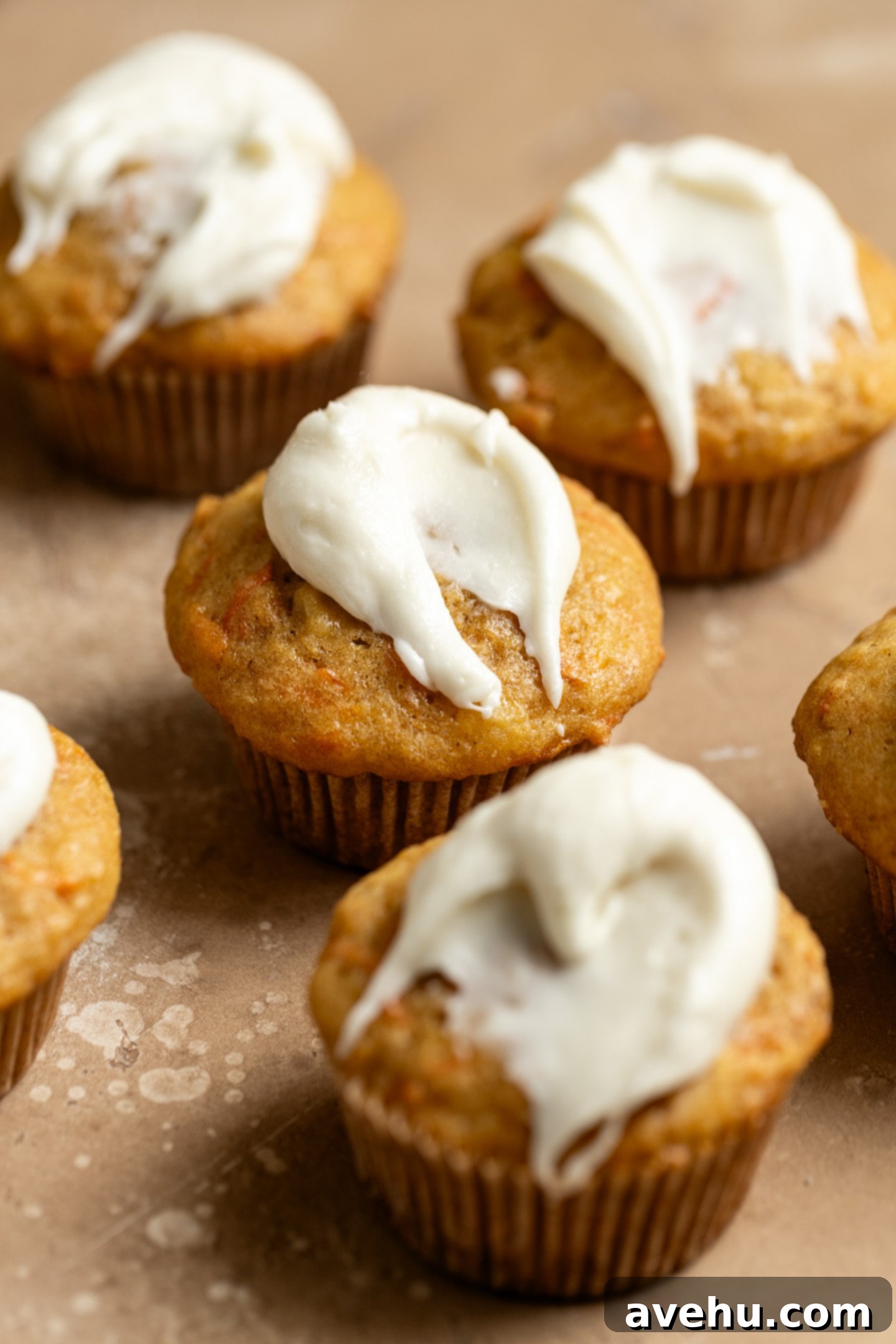Kid-Approved Carrot Pineapple Muffins 2 Moist carrot pineapple muffins generously slathered with creamy cream cheese frosting on a warm peach-colored surface.