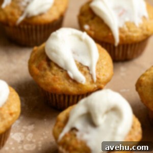Kid-Approved Carrot Pineapple Muffins 11 Carrot pineapple muffins slathered with cream cheese frosting on a peach colored surface.