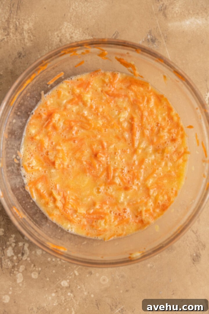 Kid-Approved Carrot Pineapple Muffins 4 Wet ingredients for moist carrot pineapple muffins in a mixing bowl, featuring shredded carrots and crushed pineapple.