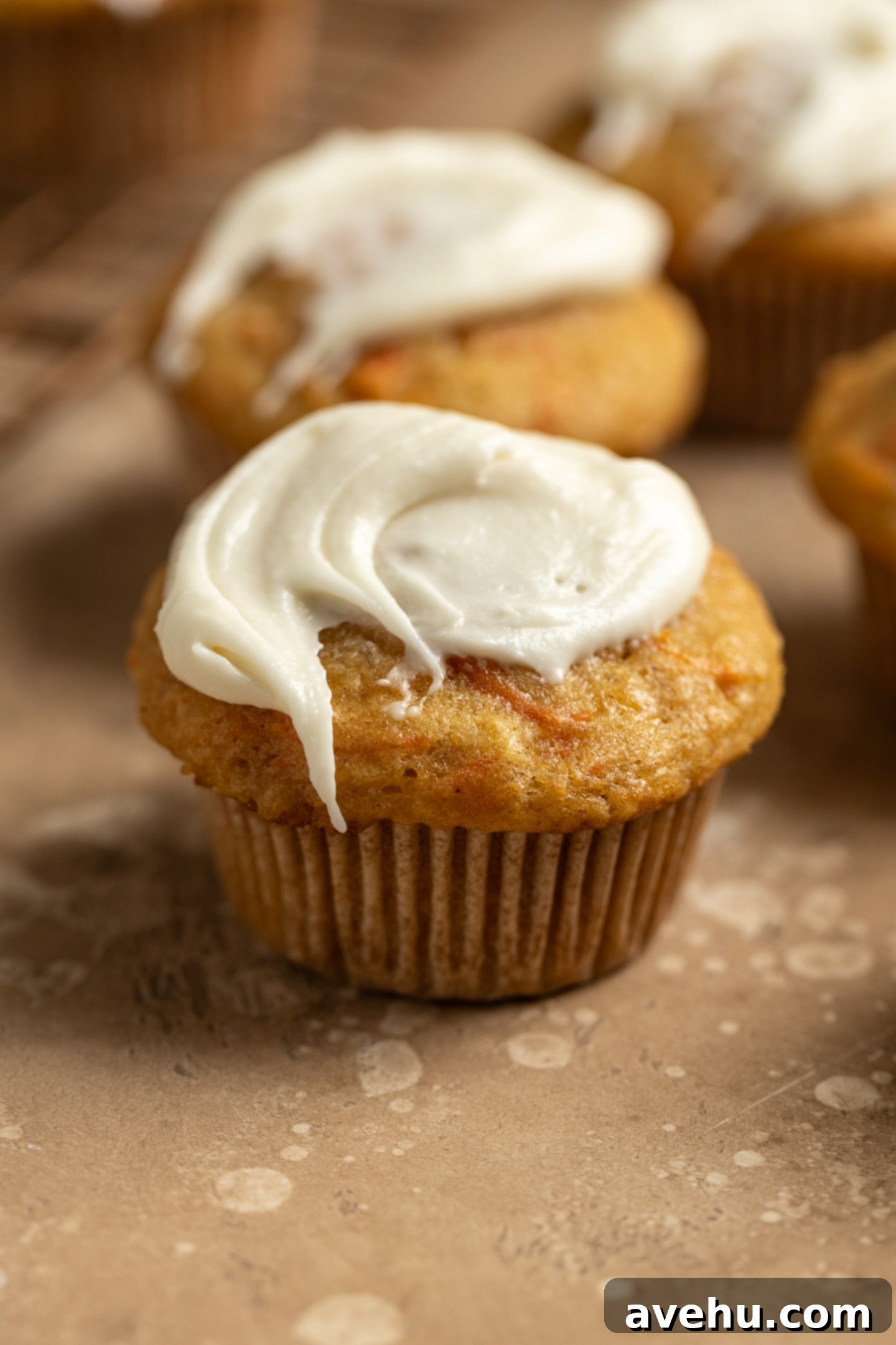 Kid-Approved Carrot Pineapple Muffins 9 A delectable carrot pineapple muffin with a generous swirl of cream cheese frosting, resting on a stylish beige surface.