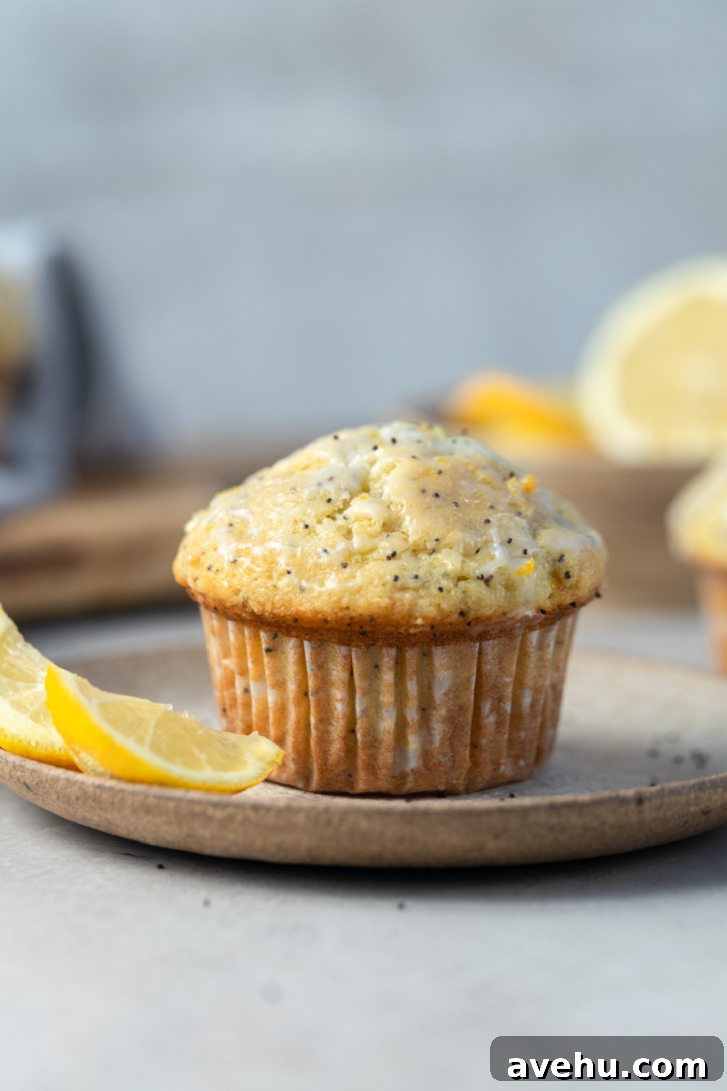 Lemon Poppy Seed Muffins Beyond Bakery Quality 2 A perfectly baked lemon poppy seed muffin, sliced in half, revealing its moist interior and evenly distributed poppy seeds. Beside it, a fresh lemon adds a pop of color to a pristine white plate.
