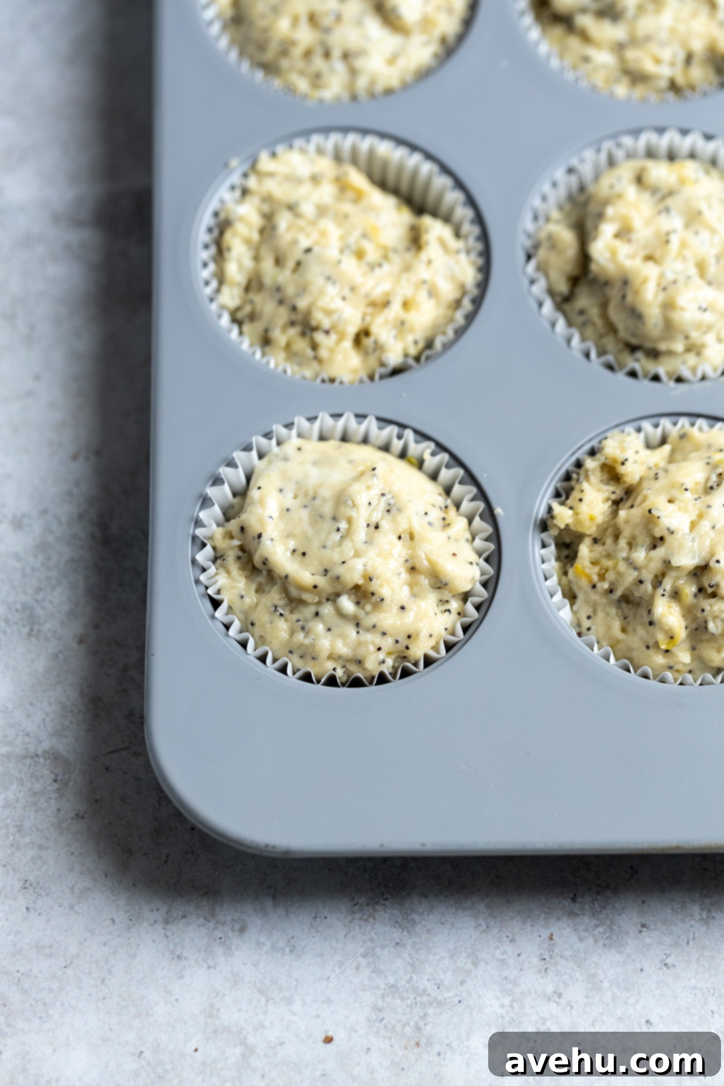 Lemon Poppy Seed Muffins Beyond Bakery Quality 7 Muffin batter generously scooped into a gray muffin tin, filling each cup to the brim, ready for baking.