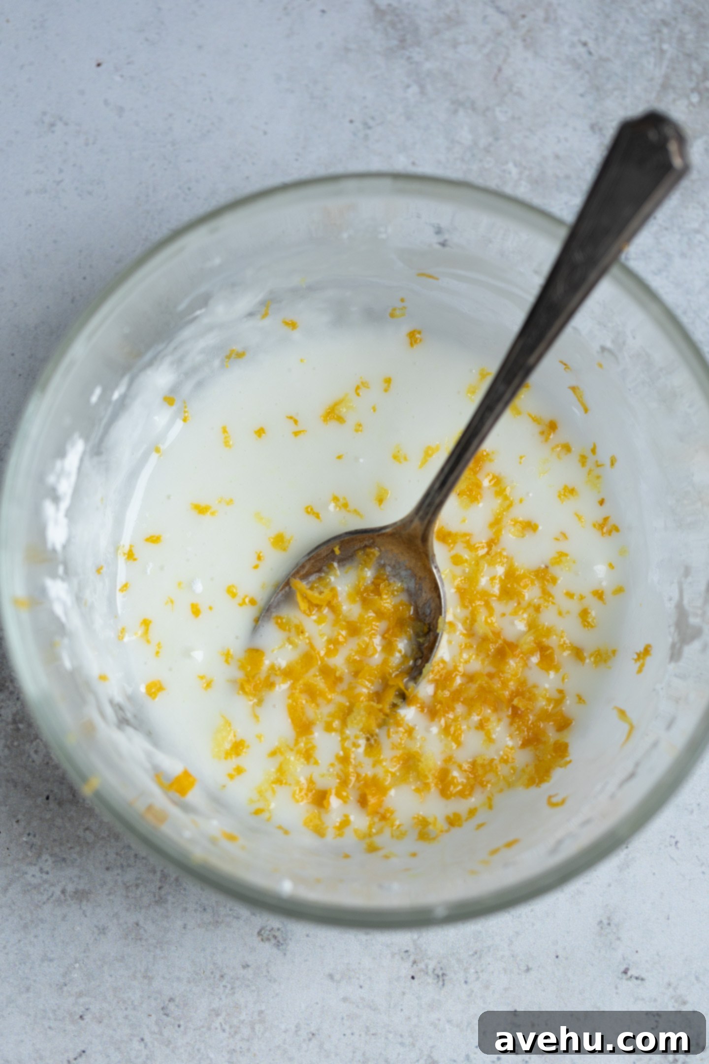 Lemon Poppy Seed Muffins Beyond Bakery Quality 8 A small glass bowl filled with a smooth, vibrant lemon glaze, subtly flecked with lemon zest, ready to be brushed onto hot muffins.