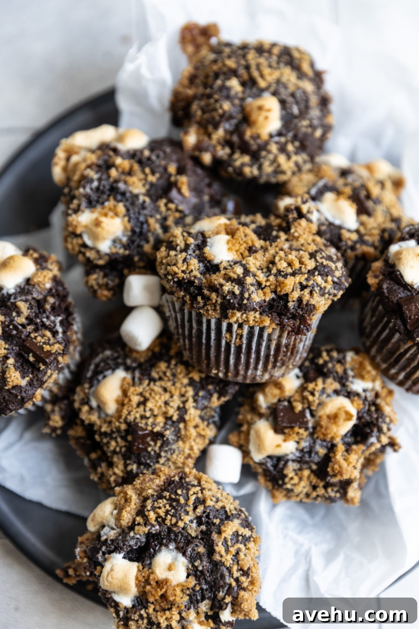 Melt-in-Your-Mouth S'mores Chocolate Muffins 2 Delicious S'mores muffins loaded with chocolate and marshmallows, topped with a golden graham cracker streusel, served in a rustic bowl.