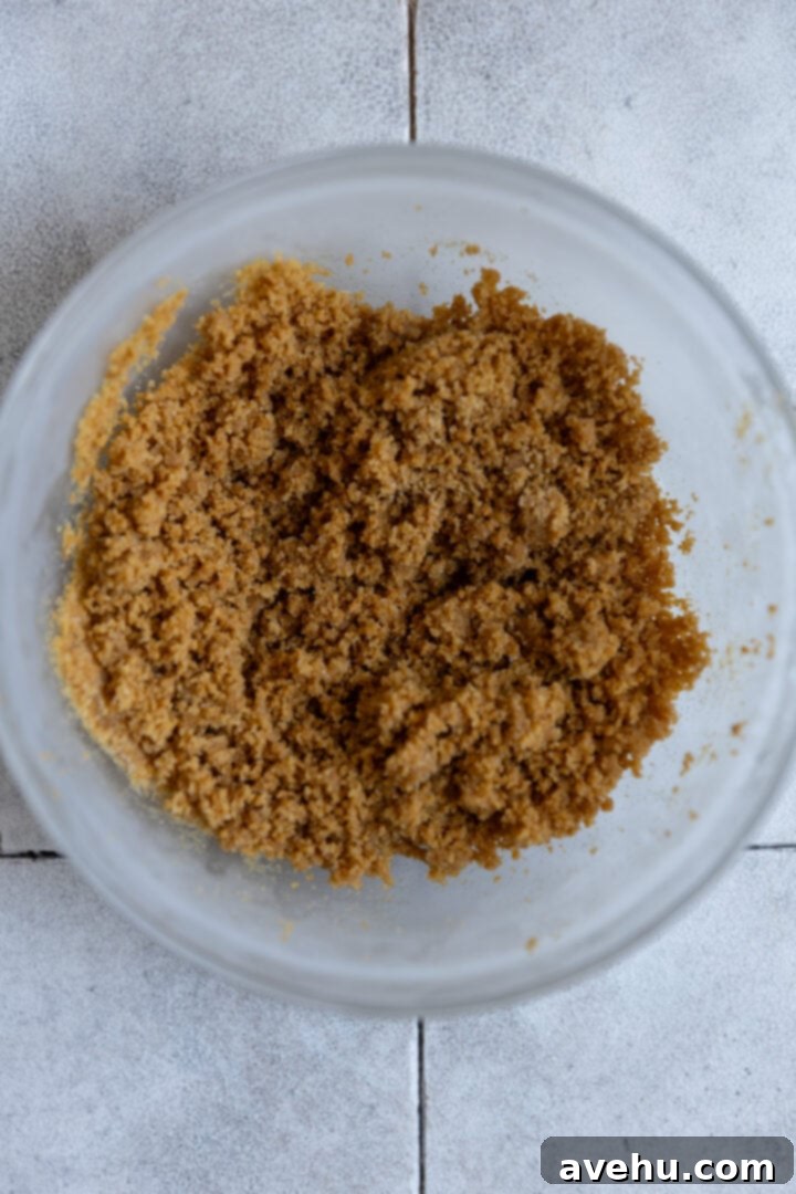 Melt-in-Your-Mouth S'mores Chocolate Muffins 3 Graham cracker streusel mixture in a clear glass bowl, showcasing its wet sand-like texture.