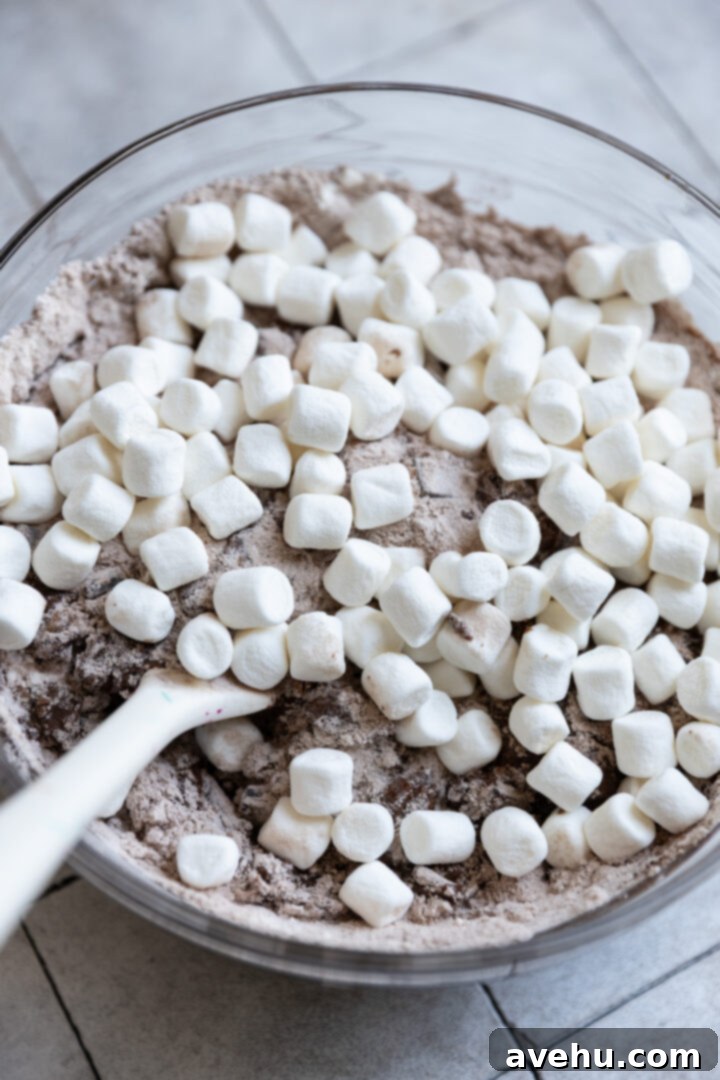 Melt-in-Your-Mouth S'mores Chocolate Muffins 7 Mini marshmallows sprinkled over S'mores muffin batter in a bowl, ready to be gently folded in.