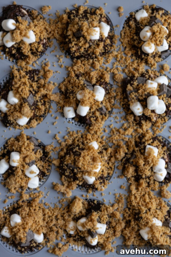 Melt-in-Your-Mouth S'mores Chocolate Muffins 8 S'mores muffin batter scooped into a muffin tin, topped with extra chocolate chunks, marshmallows, and graham cracker streusel, ready for baking.