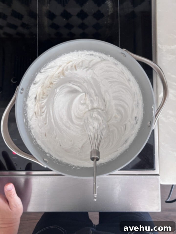 Effortless 7-Minute Frosting 7 Whipped 7 minute frosting in a pot on a stove, showing soft peaks.