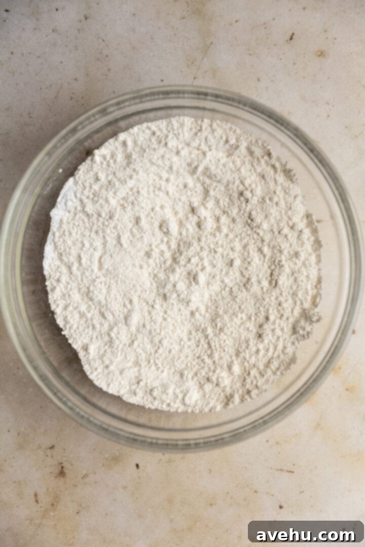 Perfectly Moist Bakery-Style Banana Muffins 4 Dry ingredients for banana muffins (flour, sugar, baking powder, baking soda, salt) in a glass bowl, whisked together.