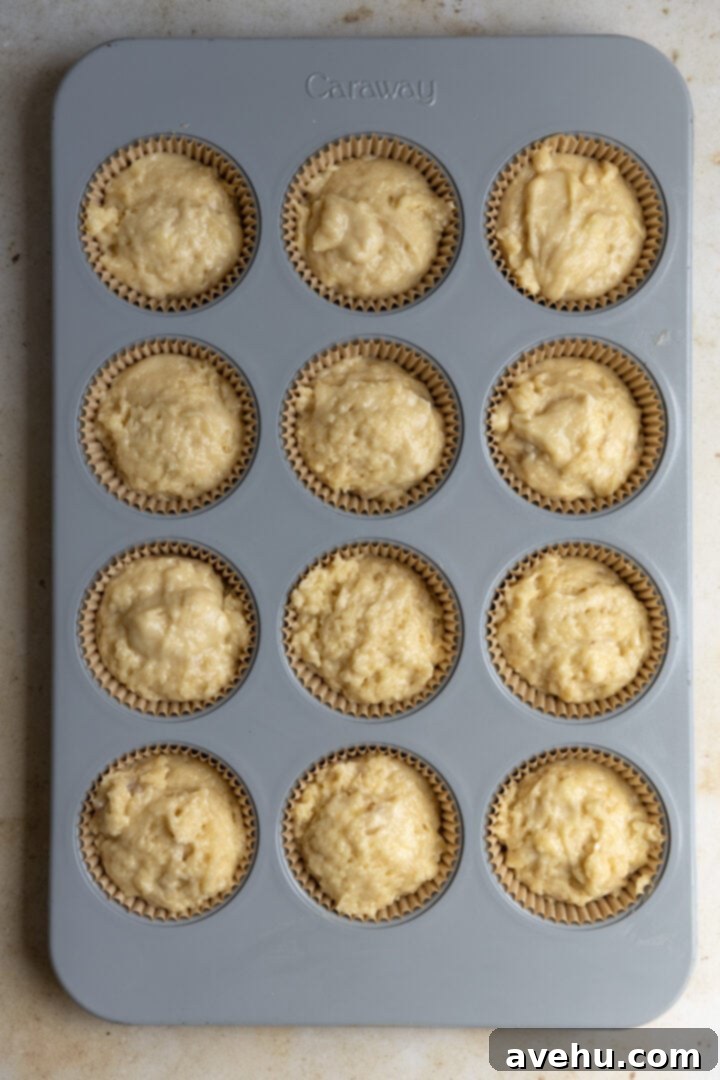 Perfectly Moist Bakery-Style Banana Muffins 7 Muffin batter filled to the brim in a 12-cup muffin tin lined with paper cups, ready for streusel and baking.