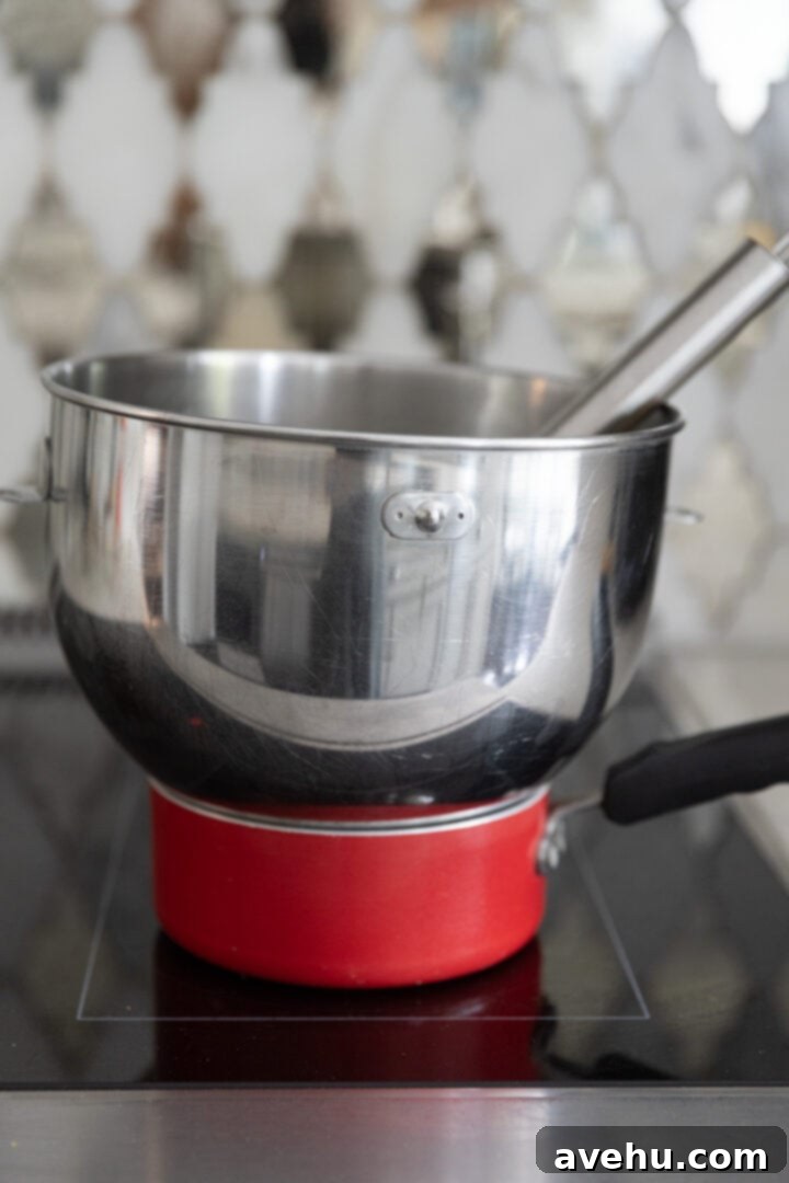 Decadent Cocoa Swiss Meringue Buttercream 3 A double boiler setup on a kitchen stove with a clean metal mixing bowl resting above simmering water.