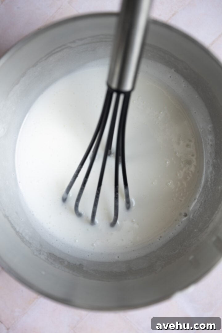 Decadent Cocoa Swiss Meringue Buttercream 4 Egg whites, granulated sugar, and cornstarch being whisked together in a mixing bowl over a double boiler, showing the initial thick texture.