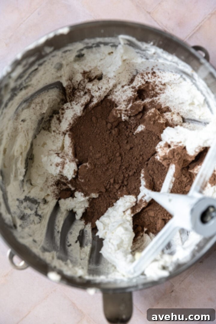 Decadent Cocoa Swiss Meringue Buttercream 9 Cocoa powder being sifted or added into a mixing bowl of smooth white Swiss meringue buttercream.
