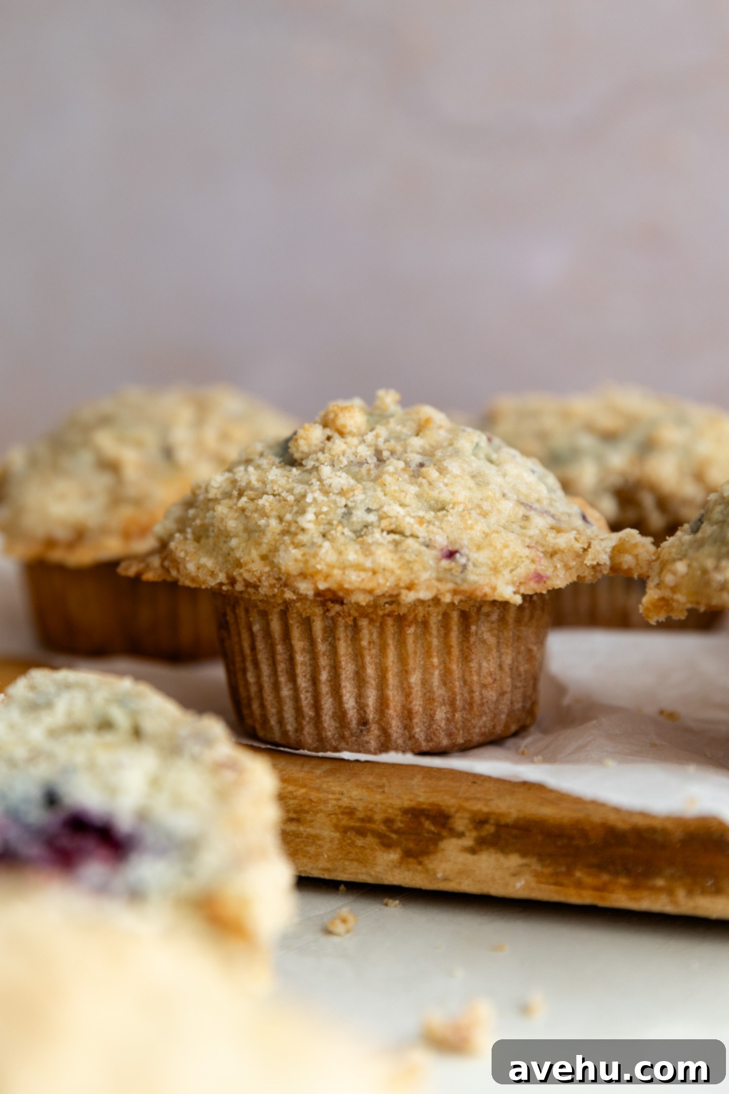 Ultimate Bakery Banana Blackberry Muffins 2 A perfectly baked banana blackberry muffin with streusel topping, sitting on a lined wooden cutting board.