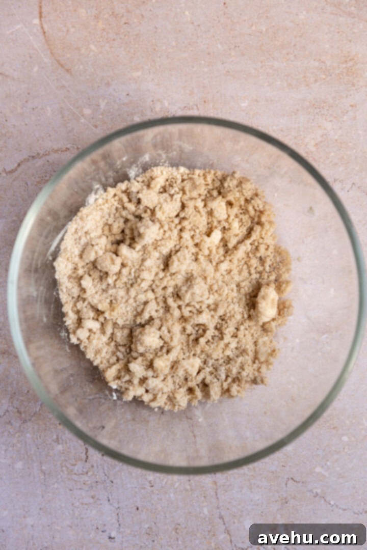 Ultimate Bakery Banana Blackberry Muffins 4 Unbaked streusel mixture, resembling wet sand with small chunks, in a glass bowl.