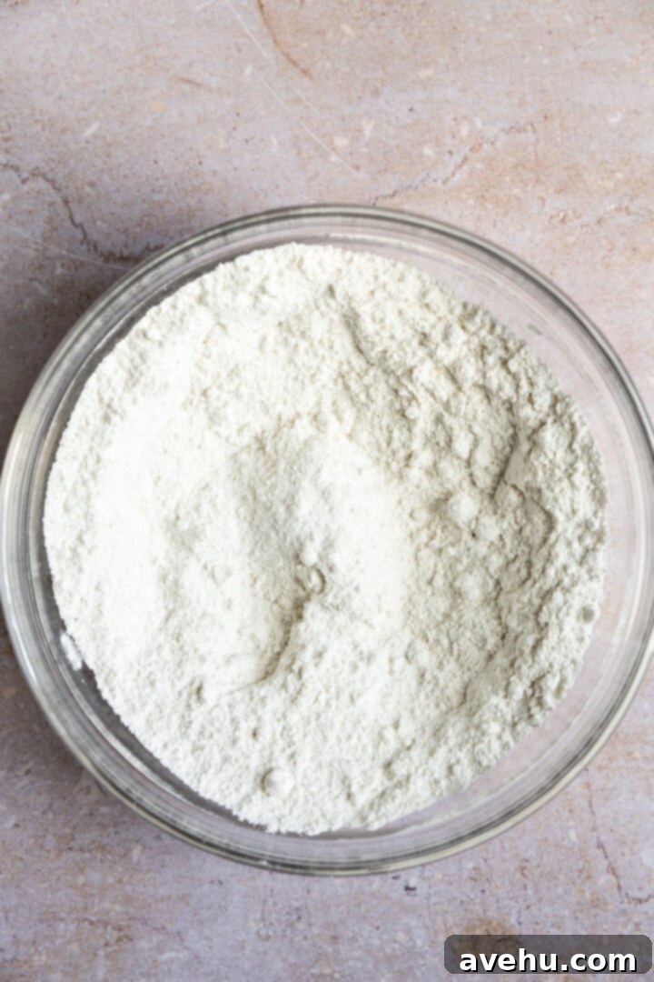 Ultimate Bakery Banana Blackberry Muffins 5 Dry ingredients for banana blackberry muffins, including flour, sugar, baking powder, baking soda, and salt, in a white bowl.