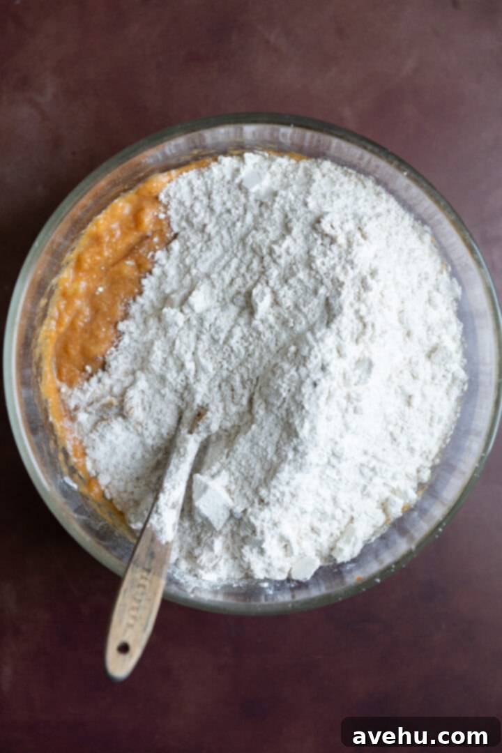 Bakery-Fresh Moist Pumpkin Banana Muffins 7 Dry ingredients carefully poured over the wet ingredients in a large glass bowl, illustrating the combining step for muffin batter.