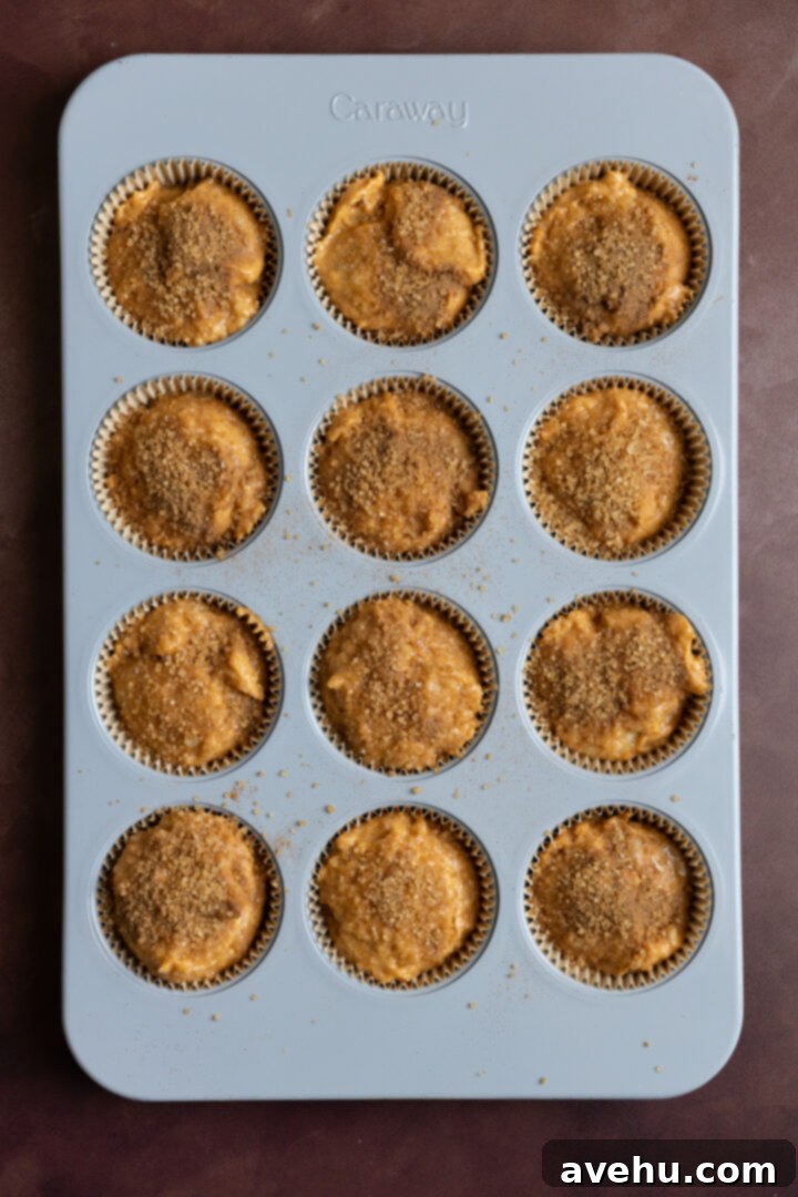 Bakery-Fresh Moist Pumpkin Banana Muffins 9 Muffin batter filled to the brim in a muffin tin, topped generously with cinnamon-sugar sprinkle, ready for baking to achieve a perfect dome.